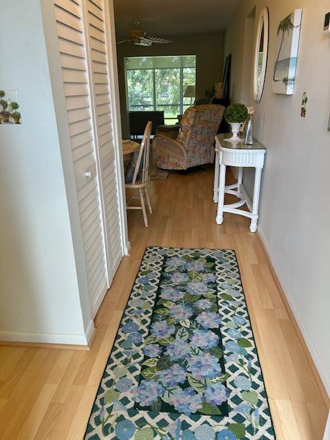 A hallway with light wood flooring and a floral runner leads to a sunlit living area — 1955 SW Palm City Road # H, Stuart FL 34994, STUART, FL
