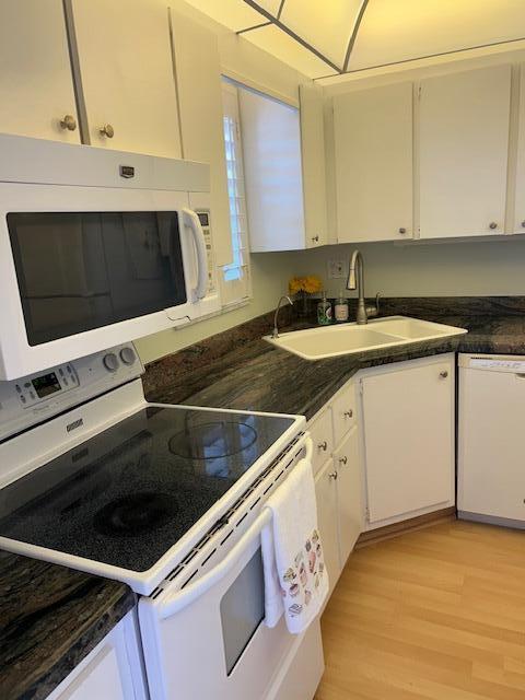A kitchen features white cabinetry, a dark granite countertop, a white stove, and a sink — 1955 SW Palm City Road # H, Stuart FL 34994, STUART, FL