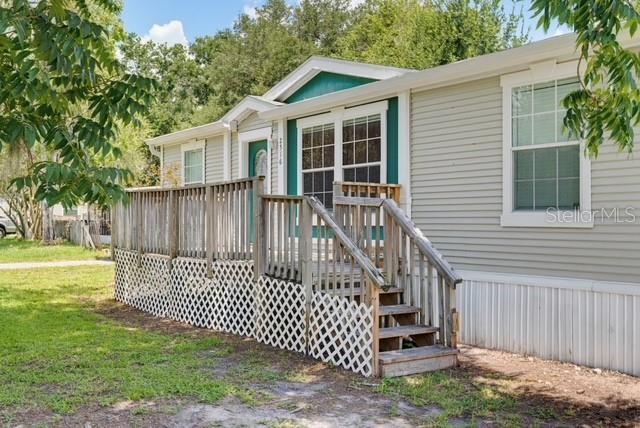 A light-colored manufactured home features a wooden deck with lattice skirting and stairs — 2516 MOBILAIRE DRIVE, LUTZ, FL