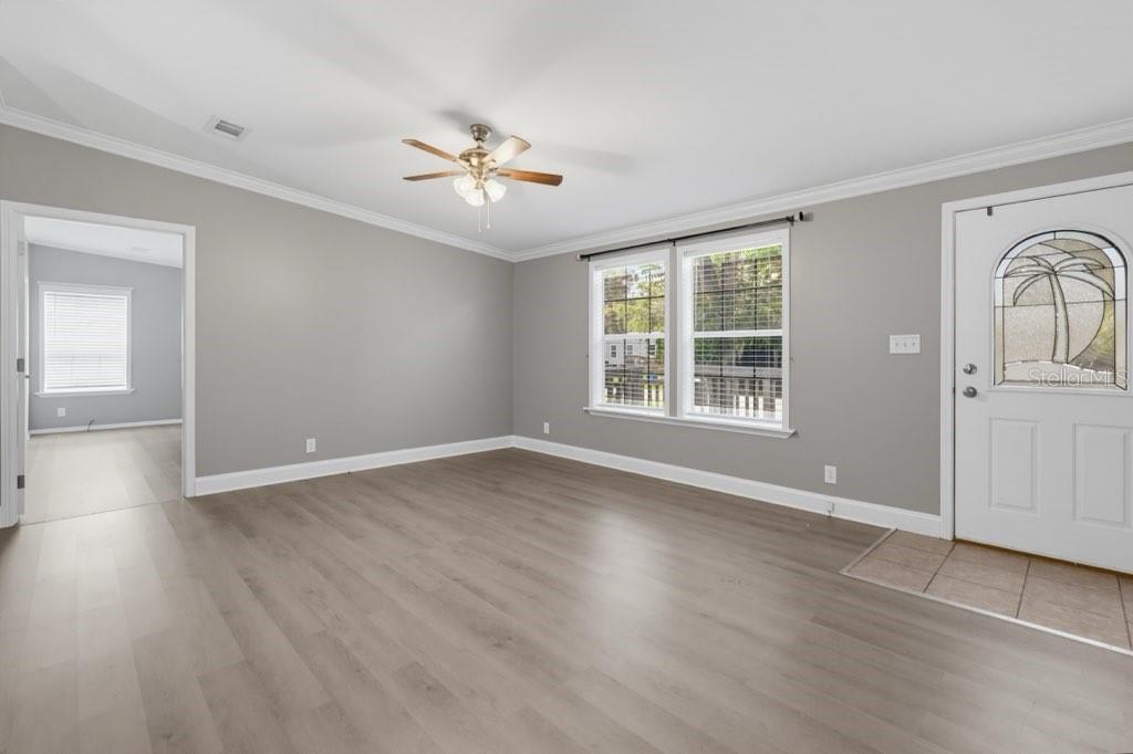 An empty living room with gray walls, light wood-look flooring, and a ceiling fan — 2516 MOBILAIRE DRIVE, LUTZ, FL