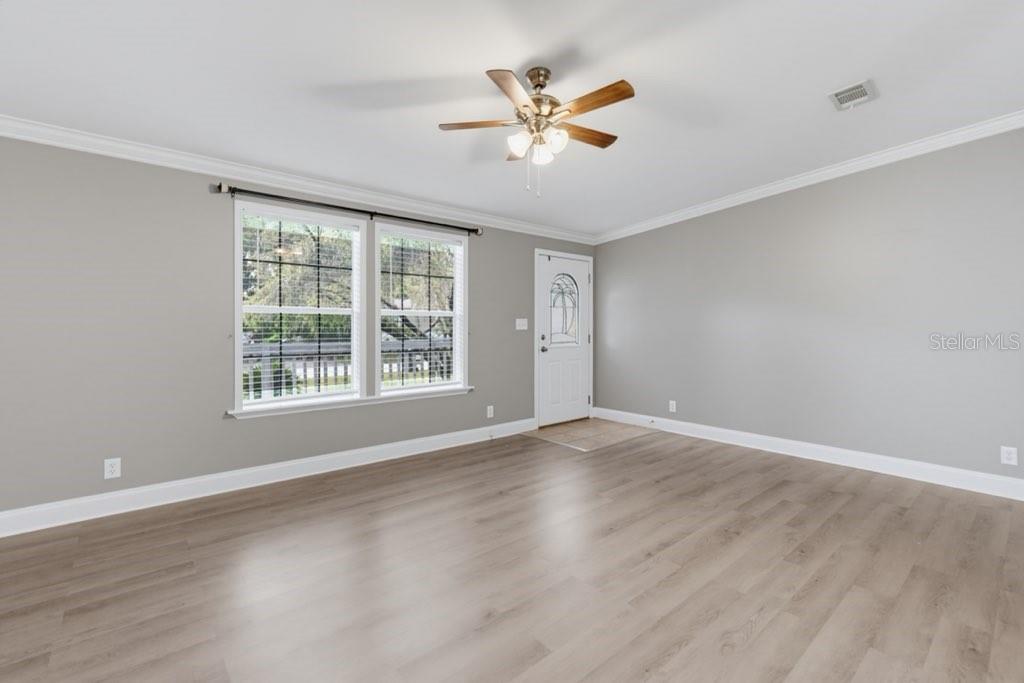 A living room with light gray walls, wood-look flooring, a ceiling fan, and a door — 2516 MOBILAIRE DRIVE, LUTZ, FL