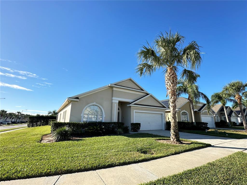 A single-story suburban house with a beige stucco exterior, a two-car garage, and palm trees — 16724 ROLLING GREEN DRIVE, CLERMONT, FL