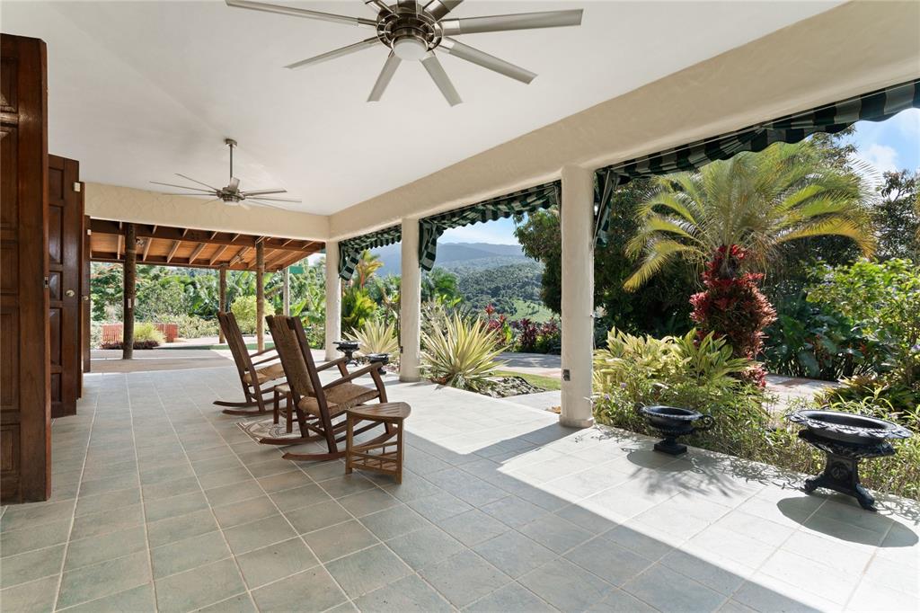 A covered patio features tiled flooring, rocking chairs, ceiling fans, and views of distant mountains — 59 REINA ISABEL, RIO GRANDE, PR