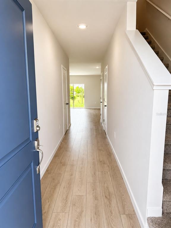 An entryway with light wood-look flooring leads to a hallway with stairs and white walls — 8201 EVERLY PRESERVE DRIVE, LEHIGH ACRES, FL