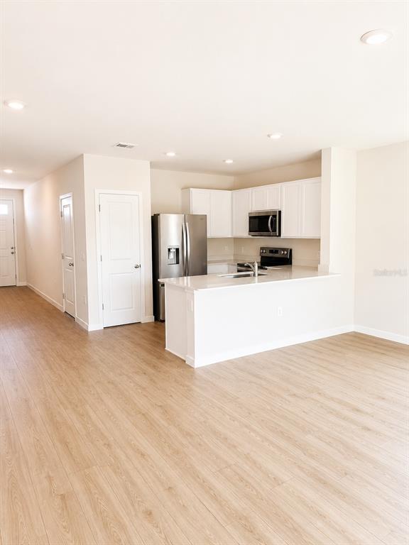 A kitchen with white cabinets, stainless steel appliances, and a peninsula island overlooks a room — 8201 EVERLY PRESERVE DRIVE, LEHIGH ACRES, FL
