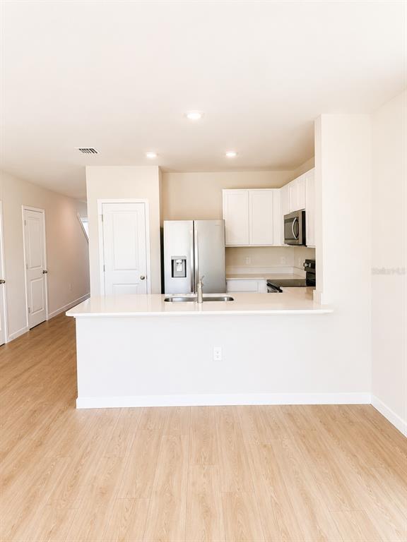 A kitchen features white cabinets, stainless steel appliances, and a peninsula with a sink — 8201 EVERLY PRESERVE DRIVE, LEHIGH ACRES, FL