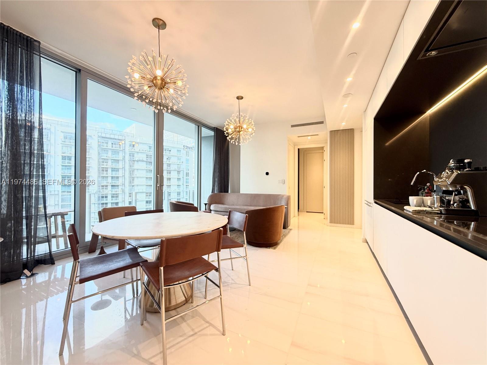A modern dining area and kitchen feature a marble table, starburst chandeliers, and floor-to-ceiling windows — 300 Biscayne Blvd Way # 3908, Miami FL 33131, MIAMI, FL