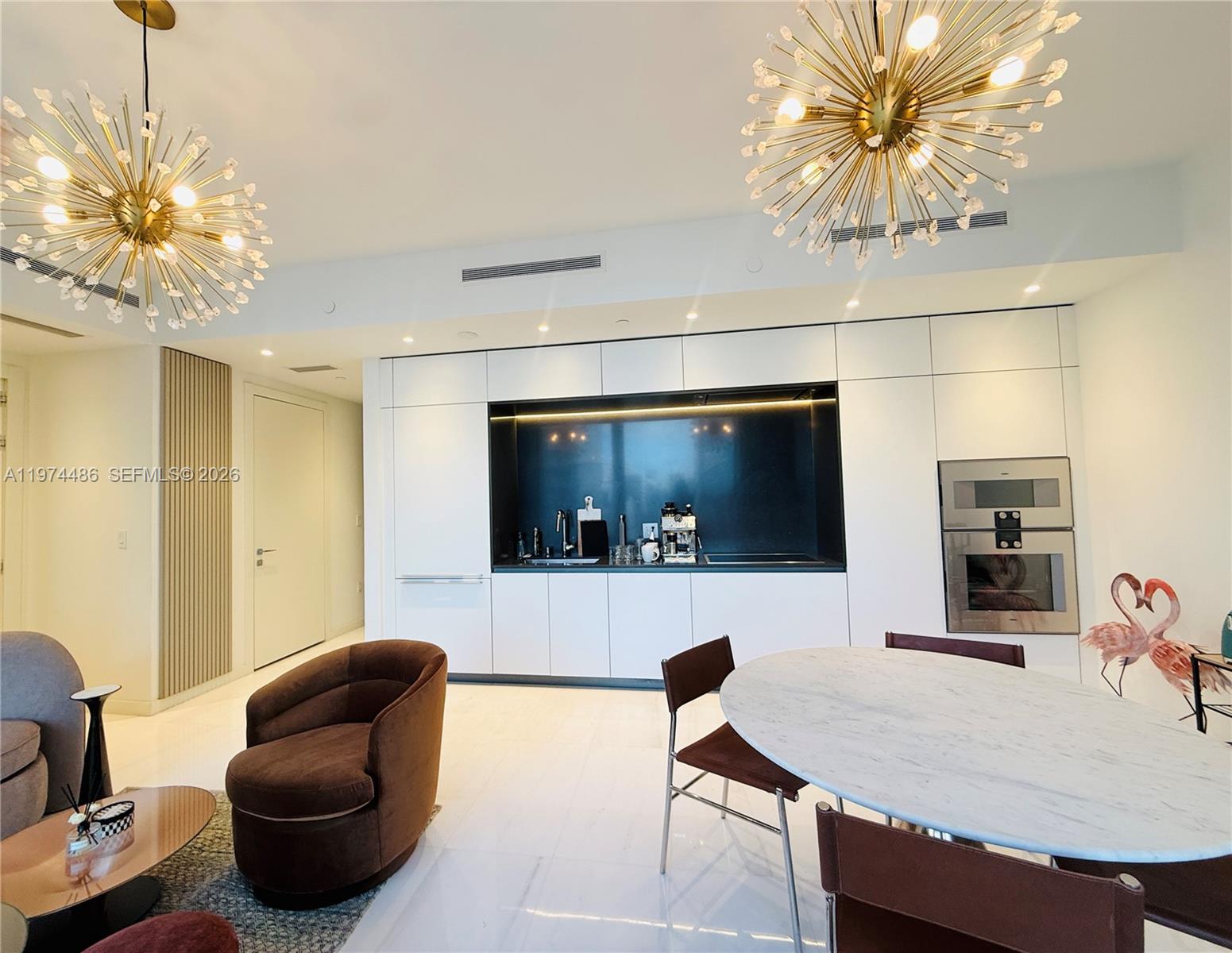 A modern kitchen features white cabinetry, a dark backsplash, and two large gold sputnik chandeliers — 300 Biscayne Blvd Way # 3908, Miami FL 33131, MIAMI, FL