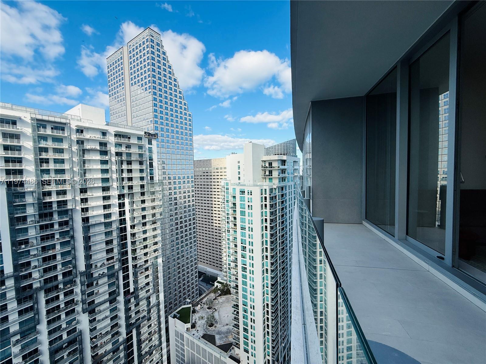 A high-rise balcony overlooks a dense urban skyline with multiple glass skyscrapers under a blue sky — 300 Biscayne Blvd Way # 3908, Miami FL 33131, MIAMI, FL