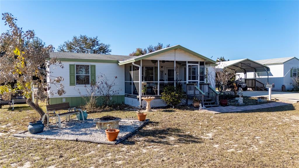 A single-story manufactured home features a screened-in front porch, a gravel fire pit area, and a carport — 708 FAZZINI ROAD, BABSON PARK, FL