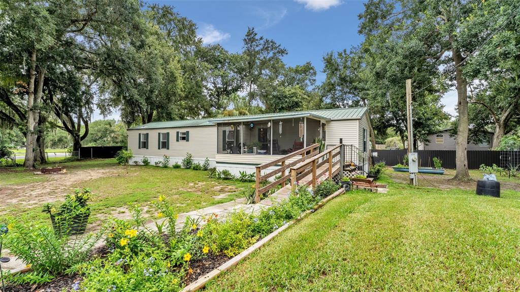 A single-story manufactured home with a screened porch and wooden ramp sits on a lawn — 2690 SHINER DRIVE, LAKE WALES, FL