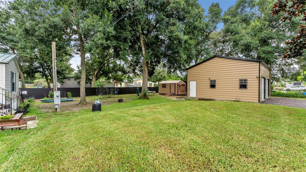 A grassy backyard features a large metal garage, a small shed, and mature trees — 2690 SHINER DRIVE, LAKE WALES, FL