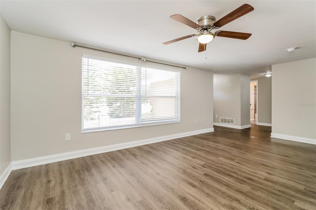 An empty room with wood-look flooring, a ceiling fan, and a large window with blinds — 7710 VENICE DRIVE, PORT RICHEY, FL
