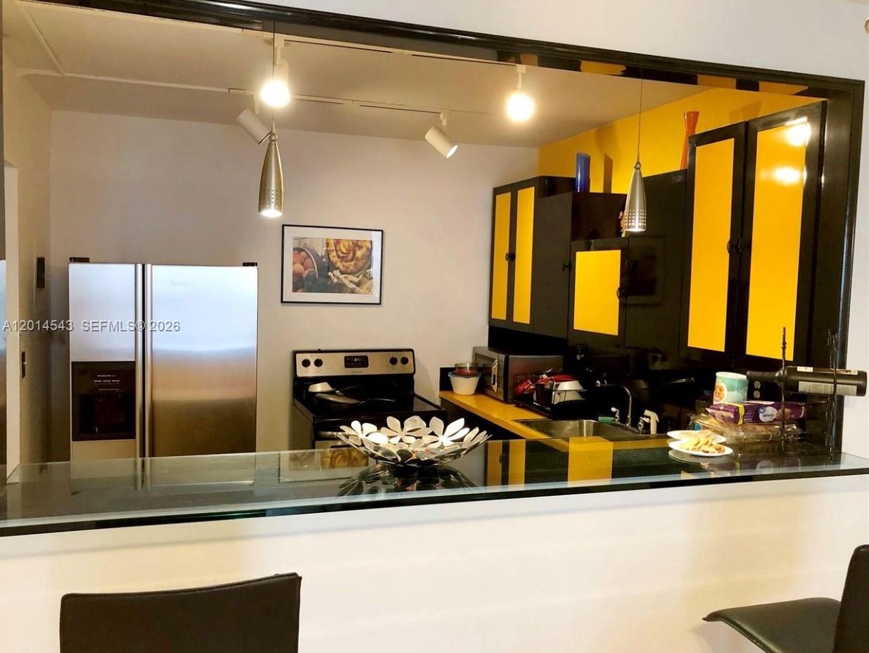 A kitchen features black cabinets with yellow accents, stainless steel appliances, and a breakfast bar — 600 Three Islands Blvd # 418, Hallandale Beach FL 33009, HALLANDALE BEACH, FL