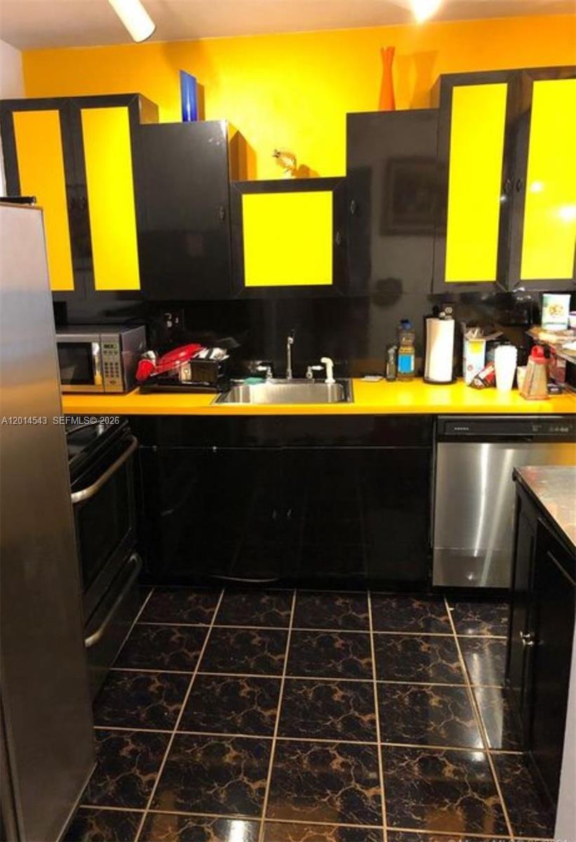 A kitchen features black cabinets with yellow accents, a yellow countertop, and dark tiled flooring — 600 Three Islands Blvd # 418, Hallandale Beach FL 33009, HALLANDALE BEACH, FL