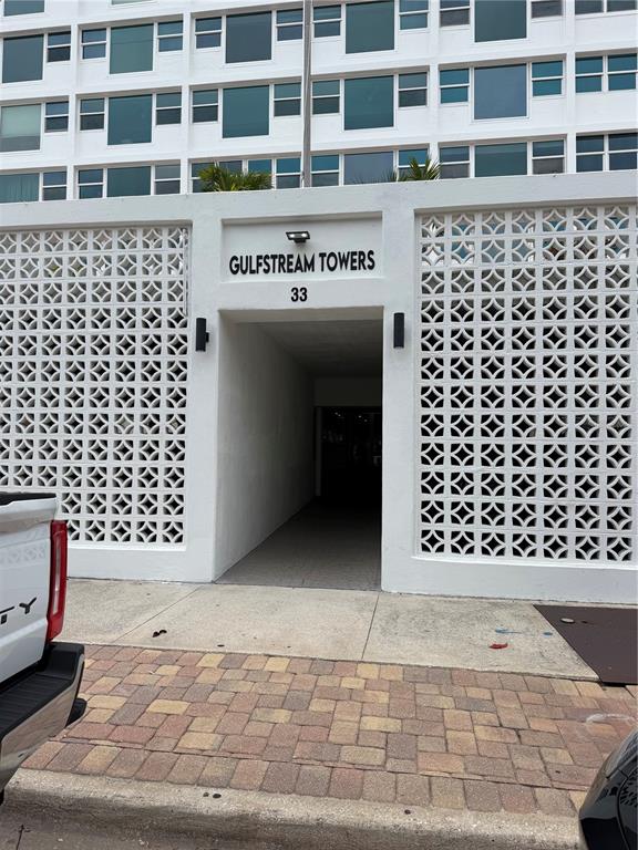 The exterior entrance of Gulfstream Towers features a white concrete facade with decorative block walls — 33 S GULFSTREAM AVENUE UNIT 1001, SARASOTA, FL