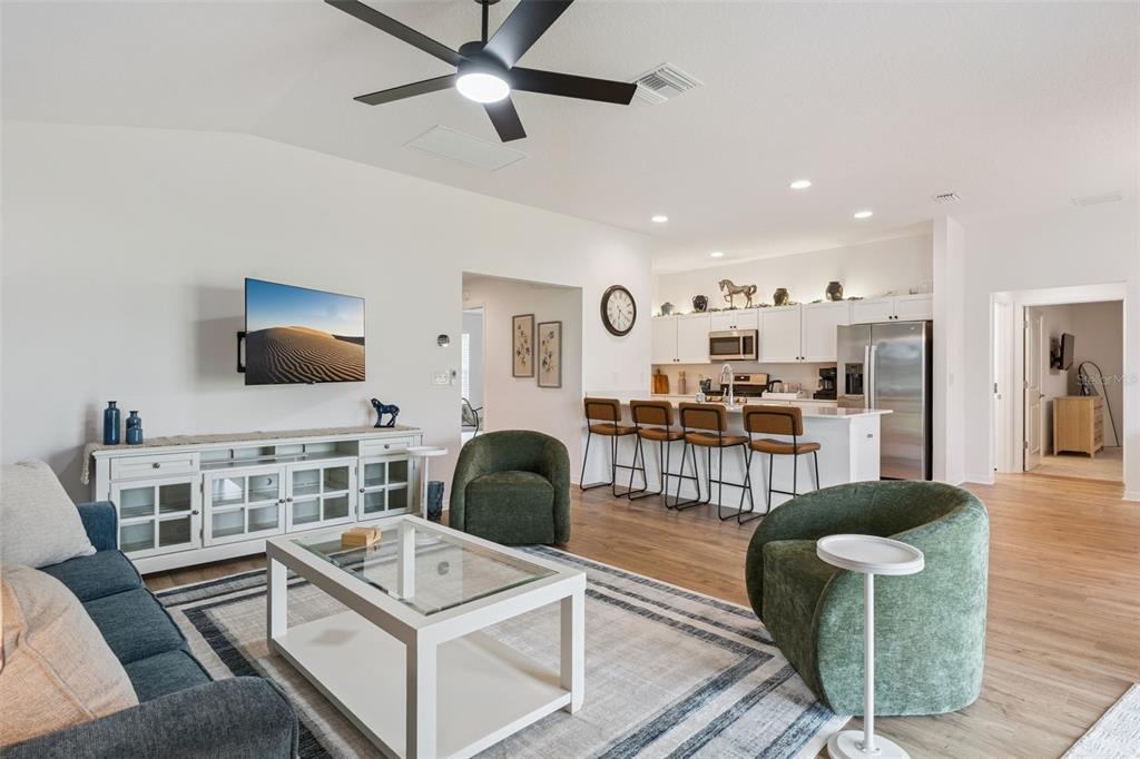 A living room with a blue sofa, two green chairs, and an open kitchen island — 7608 DANIEL HEARNS WAY, THE VILLAGES, FL