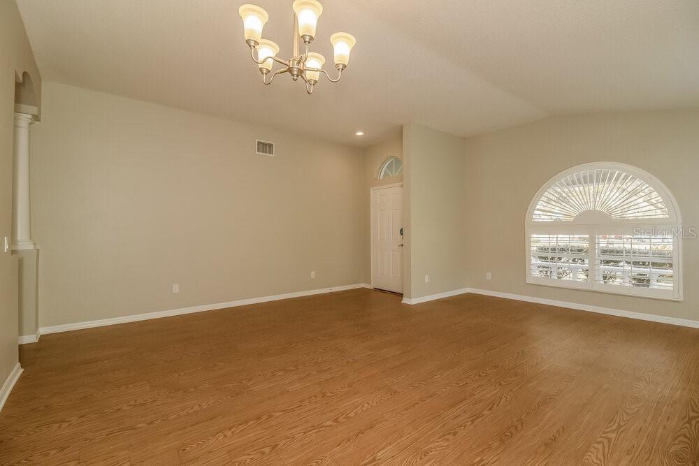 An empty room with light-colored walls, wood-look flooring, a chandelier, and an arched window — 633 STRAW LAKE DRIVE, BRANDON, FL