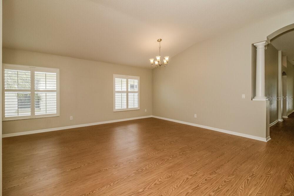 An empty room with light-colored walls, wood-look flooring, two windows with shutters, and a chandelier — 633 STRAW LAKE DRIVE, BRANDON, FL