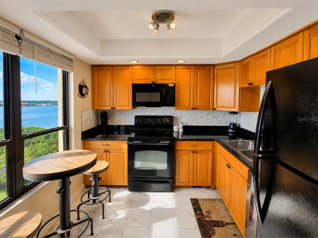A kitchen with wood cabinets, black appliances, granite countertops, and a view of the water — 2616 COVE CAY DRIVE UNIT 801, CLEARWATER, FL