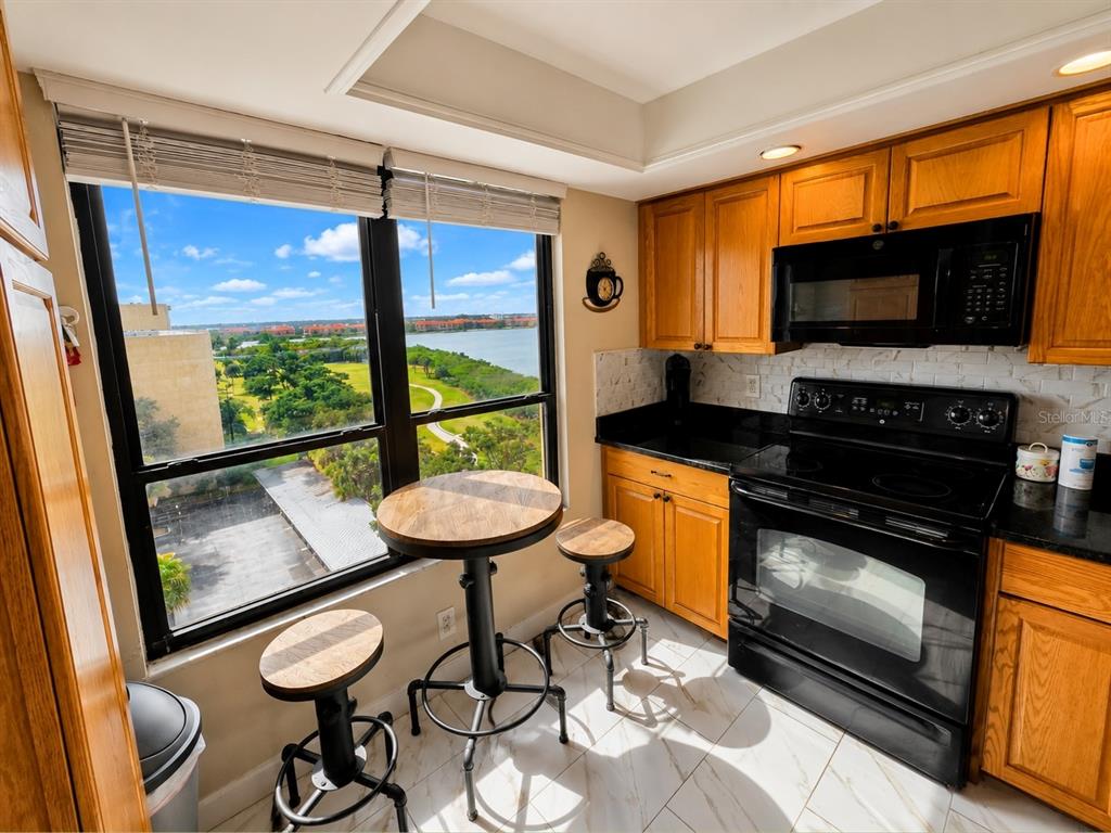 A kitchen with wooden cabinets, black appliances, and a small dining table by a window — 2616 COVE CAY DRIVE UNIT 801, CLEARWATER, FL
