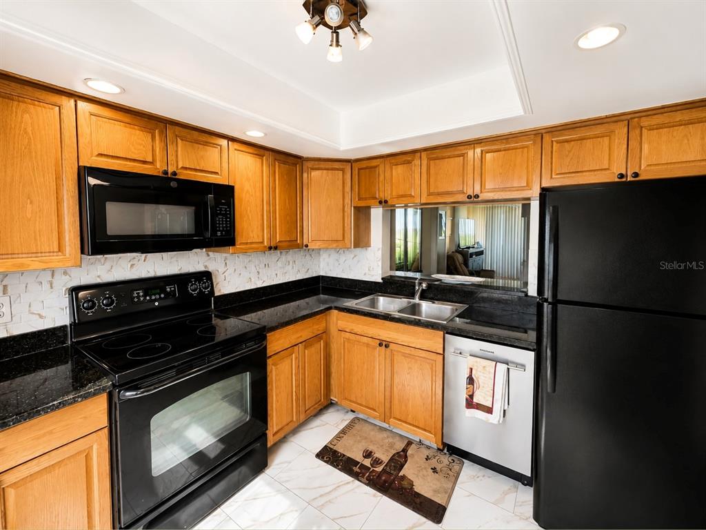 A kitchen features oak cabinets, black appliances, dark granite countertops, and white tile flooring — 2616 COVE CAY DRIVE UNIT 801, CLEARWATER, FL