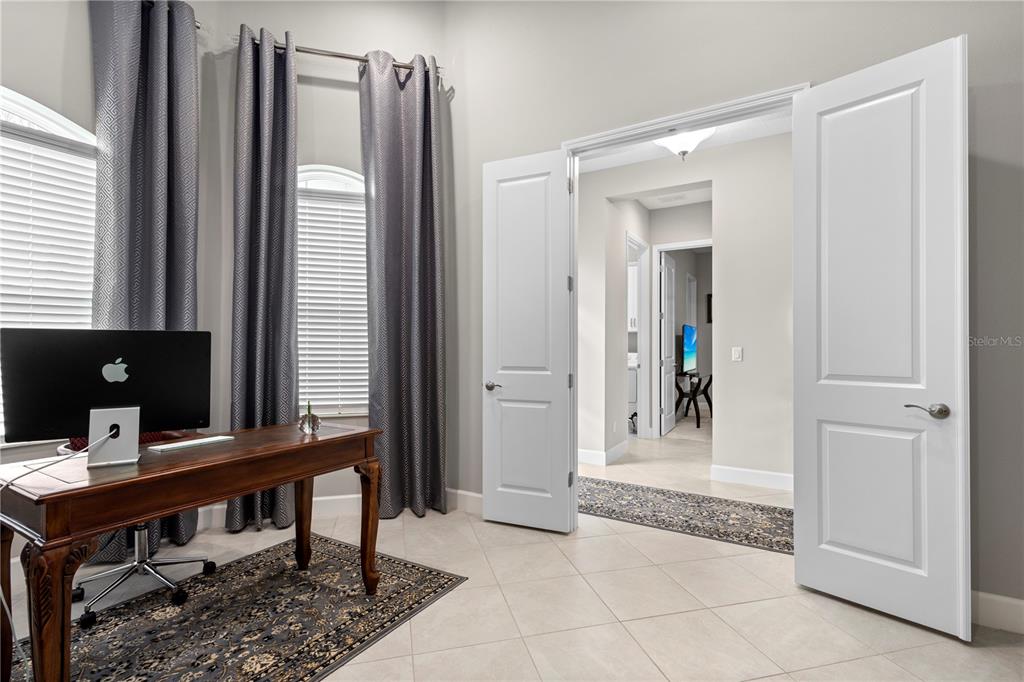 A home office features a wooden desk, a computer, grey curtains, and double doors — 4839 SEVILLA SHORES DRIVE, WIMAUMA, FL