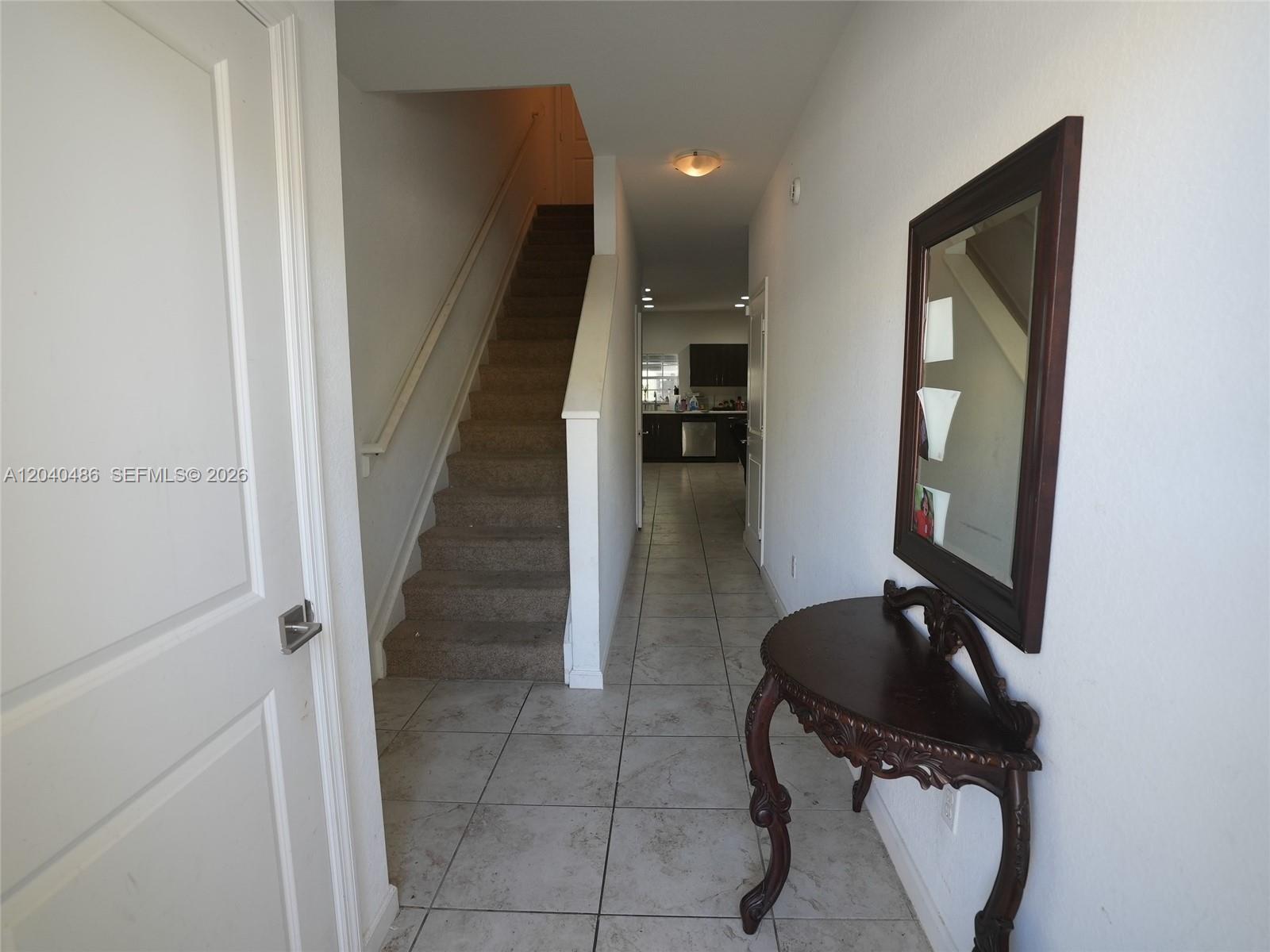 A hallway with tile flooring leads to a kitchen, featuring a staircase and console table — 4037 NW 10th Pl, Lauderhill FL 33313, LAUDERHILL, FL