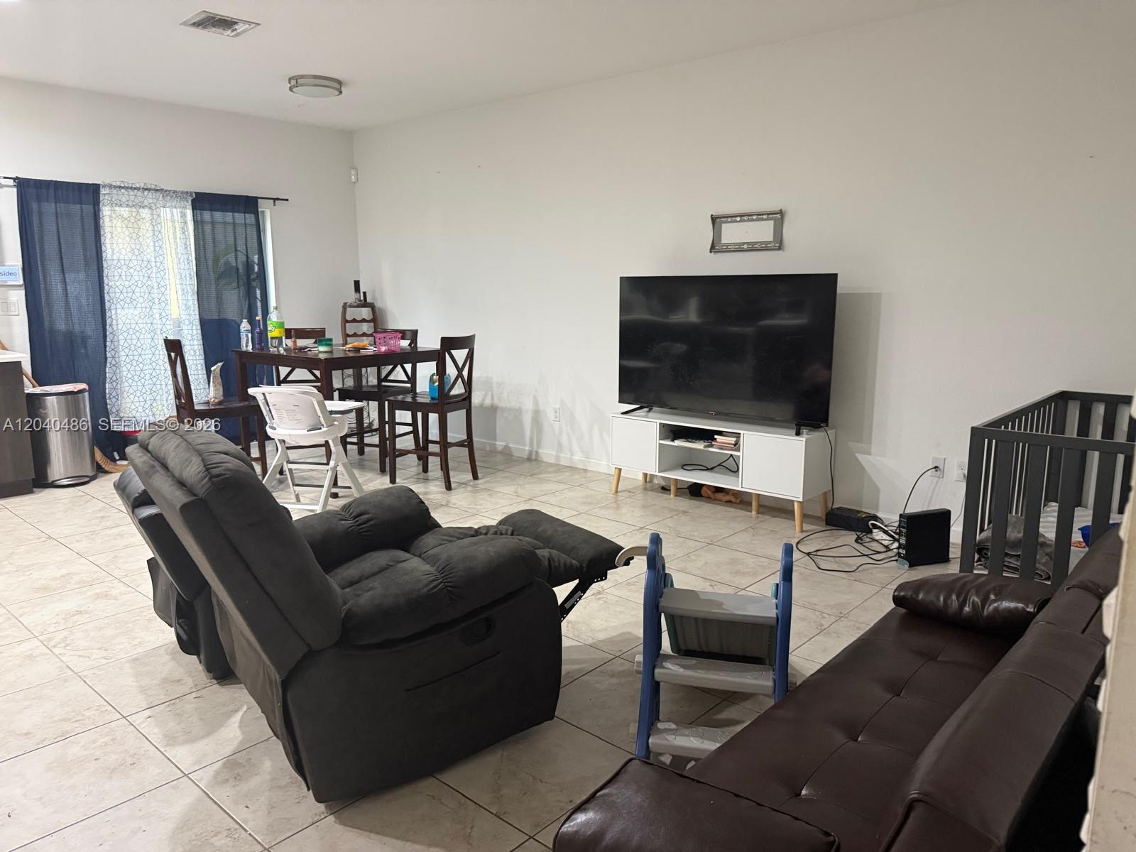 A living room with tile floors, a television on a white stand, and dining furniture — 4037 NW 10th Pl, Lauderhill FL 33313, LAUDERHILL, FL