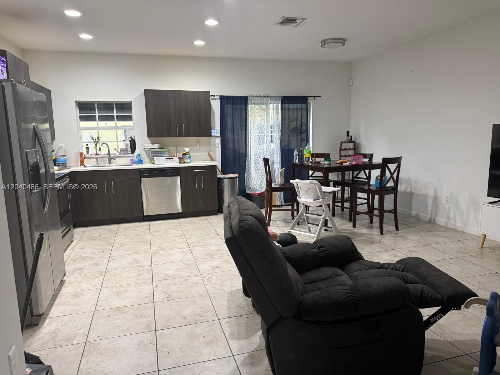 An open-concept kitchen and dining area features dark wood cabinetry, tile flooring, and a recliner — 4037 NW 10th Pl, Lauderhill FL 33313, LAUDERHILL, FL