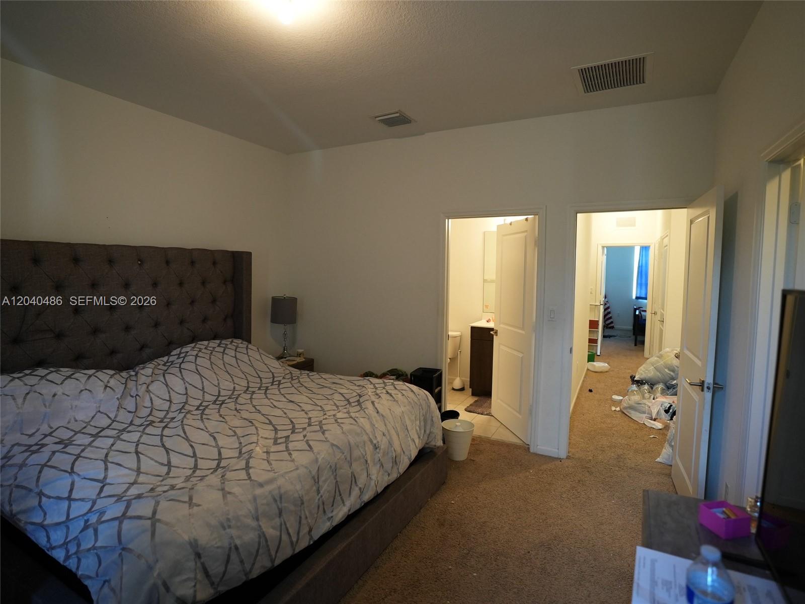 A bedroom features a tufted headboard, a patterned comforter, and two doorways leading to other rooms — 4037 NW 10th Pl, Lauderhill FL 33313, LAUDERHILL, FL