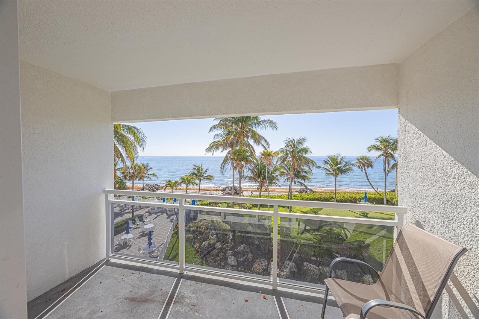 A balcony with a glass railing overlooks a grassy area, palm trees, and the ocean — 500 SE 21st Avenue # 403, Deerfield Beach FL 33441, DEERFIELD BEACH, FL