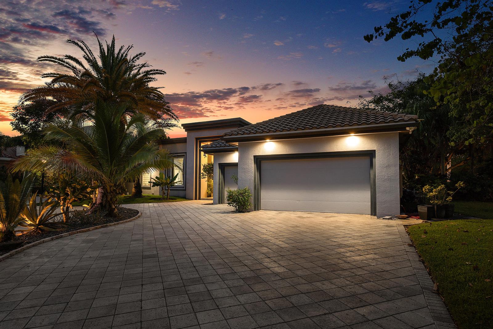 A single-story house with a paved driveway, a two-car garage, and a palm tree at dusk — 6595 NW 32nd Terrace, Boca Raton FL 33496, BOCA RATON, FL