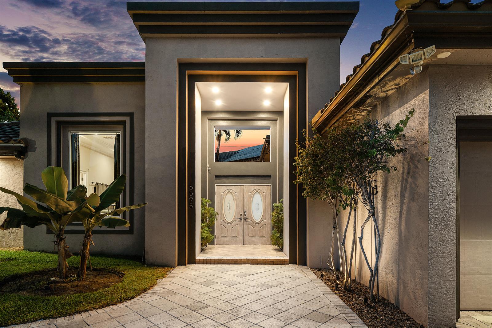 The exterior of a modern home features a recessed entryway with double doors and landscaping — 6595 NW 32nd Terrace, Boca Raton FL 33496, BOCA RATON, FL