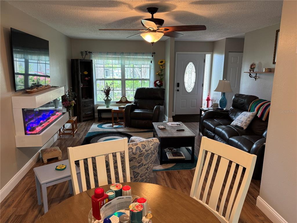 A living room features a fireplace, dark leather furniture, a ceiling fan, and wood flooring — 10707 SALAMANCA DRIVE, PORT RICHEY, FL