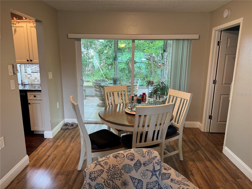 A dining area features a round wooden table with white chairs, wood-look flooring, and sliding glass doors — 10707 SALAMANCA DRIVE, PORT RICHEY, FL