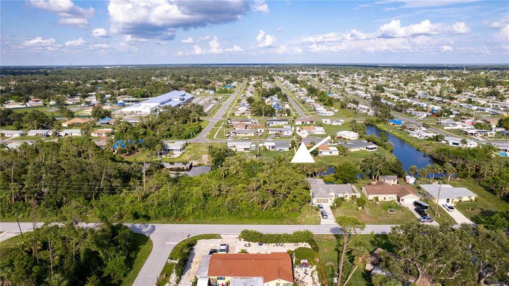 An aerial view shows a residential neighborhood with houses, a canal, and surrounding vegetation — 1556 BIRCHCREST BOULEVARD, PORT CHARLOTTE, FL