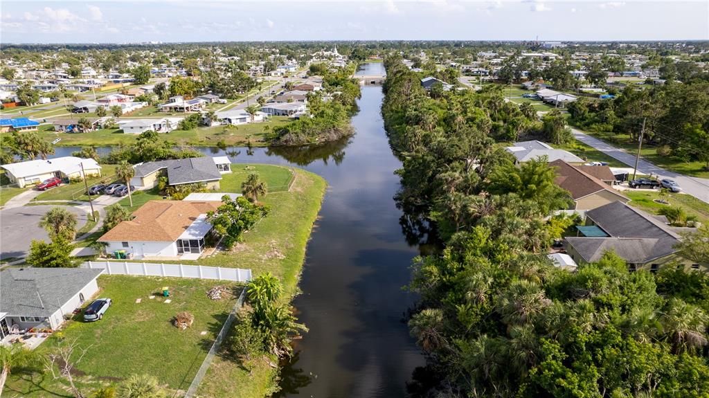 An aerial view shows a canal flowing between residential houses and dense green vegetation — 1556 BIRCHCREST BOULEVARD, PORT CHARLOTTE, FL