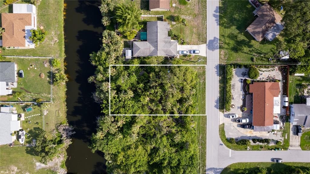 An aerial view shows a rectangular wooded lot situated between a canal and a road — 1556 BIRCHCREST BOULEVARD, PORT CHARLOTTE, FL