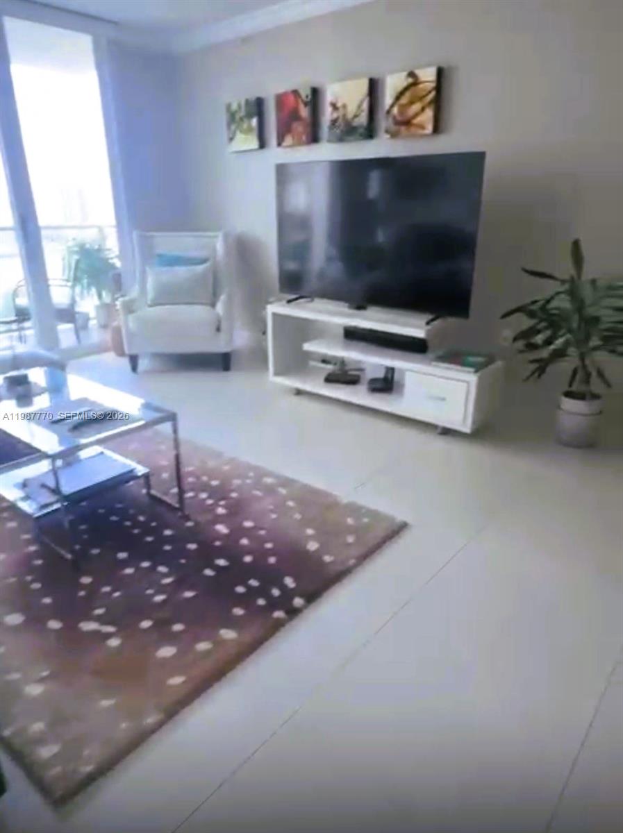 A living room features a television on a white stand, a patterned rug, and seating — 1155 Brickell Bay Dr # 1008, Miami FL 33131, MIAMI, FL