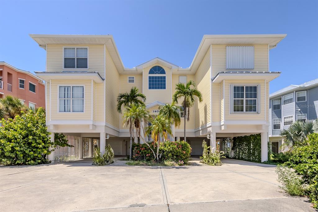 A yellow, elevated multi-story house with a concrete driveway and palm trees in front — 1400 BEACH ROAD UNIT 3, ENGLEWOOD, FL