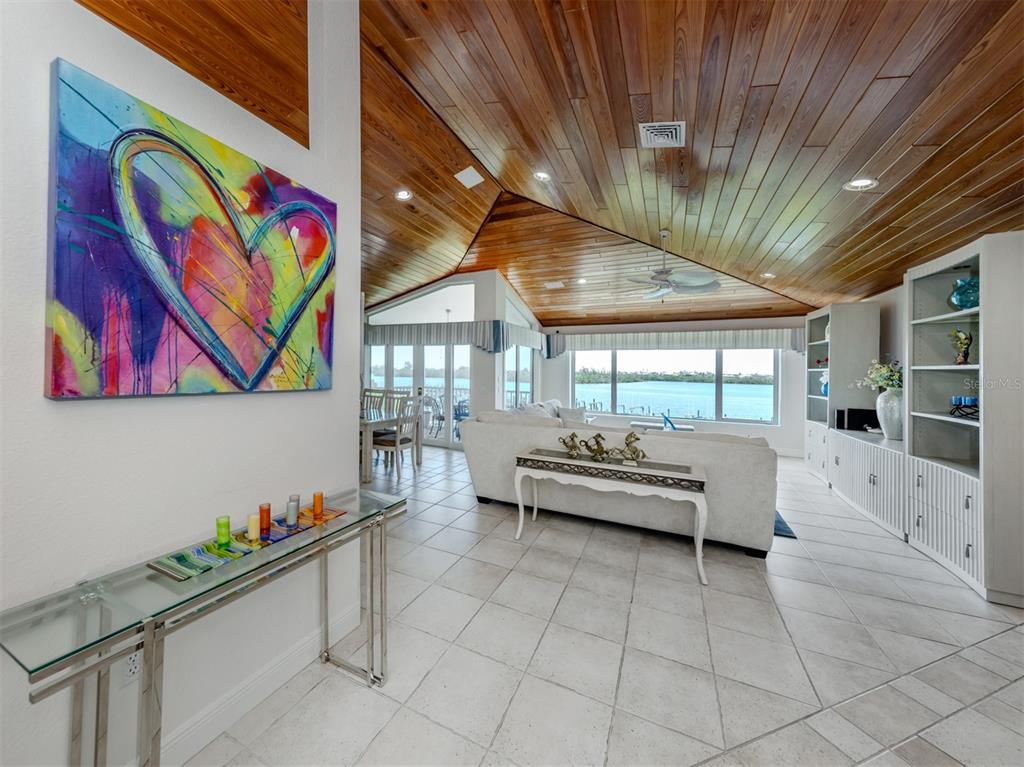 A living room features a wood-paneled vaulted ceiling, tile flooring, and a view of water — 1400 BEACH ROAD UNIT 3, ENGLEWOOD, FL