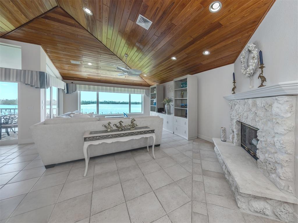 A living room features a vaulted wood-plank ceiling, stone fireplace, and views of the water — 1400 BEACH ROAD UNIT 3, ENGLEWOOD, FL