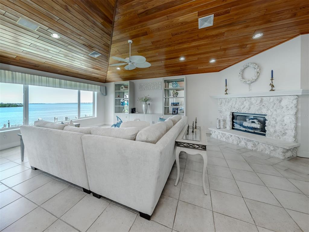 A living room features a vaulted wood-paneled ceiling, white stone fireplace, and panoramic water views — 1400 BEACH ROAD UNIT 3, ENGLEWOOD, FL