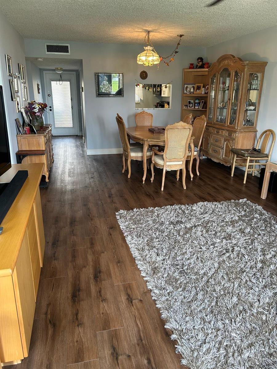 A dining area with a wooden table and chairs sits adjacent to a living room — 6670 Royal Palm Boulevard # 112k, Margate FL 33063, MARGATE, FL