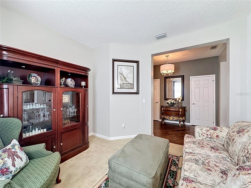 A living room features a large wooden hutch, a floral sofa, and a green ottoman — 395 SILVER MAPLE ROAD, GROVELAND, FL