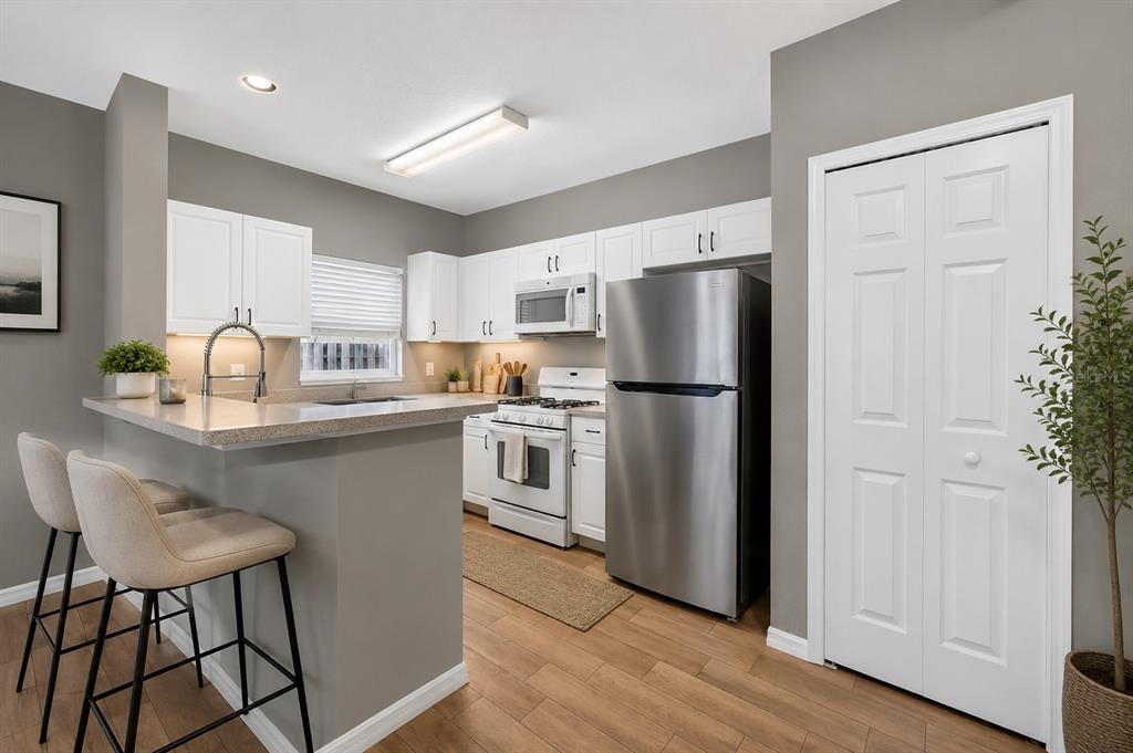 A kitchen with white cabinets, stainless steel appliances, and a breakfast bar with two stools — 15032 DEER MEADOW DRIVE, LUTZ, FL
