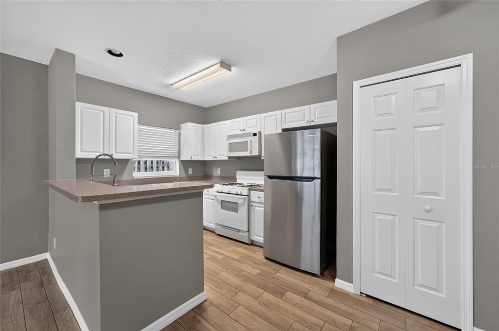 A kitchen with white cabinets, stainless steel appliances, and a breakfast bar on wood flooring — 15032 DEER MEADOW DRIVE, LUTZ, FL
