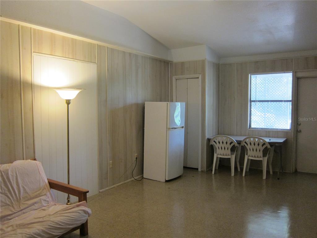 A room with wood-paneled walls, a refrigerator, a floor lamp, and a small dining area — 1602 SW WILLISTON ROAD UNIT A, GAINESVILLE, FL