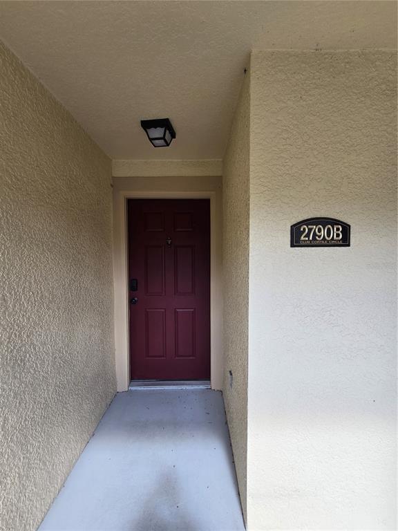A red front door is set within a recessed entryway with beige stucco walls — 2790 CLUB CORTILE CIRCLE UNIT B, KISSIMMEE, FL